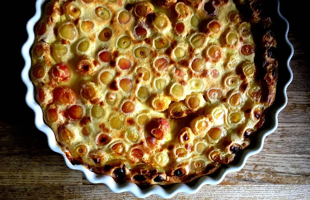 Un d&eacute;licieux clafoutis aux cerises, dor&eacute; et gonfl&eacute;, dans un plat blanc festonn&eacute;, pr&ecirc;t &agrave; &ecirc;tre d&eacute;gust&eacute;.