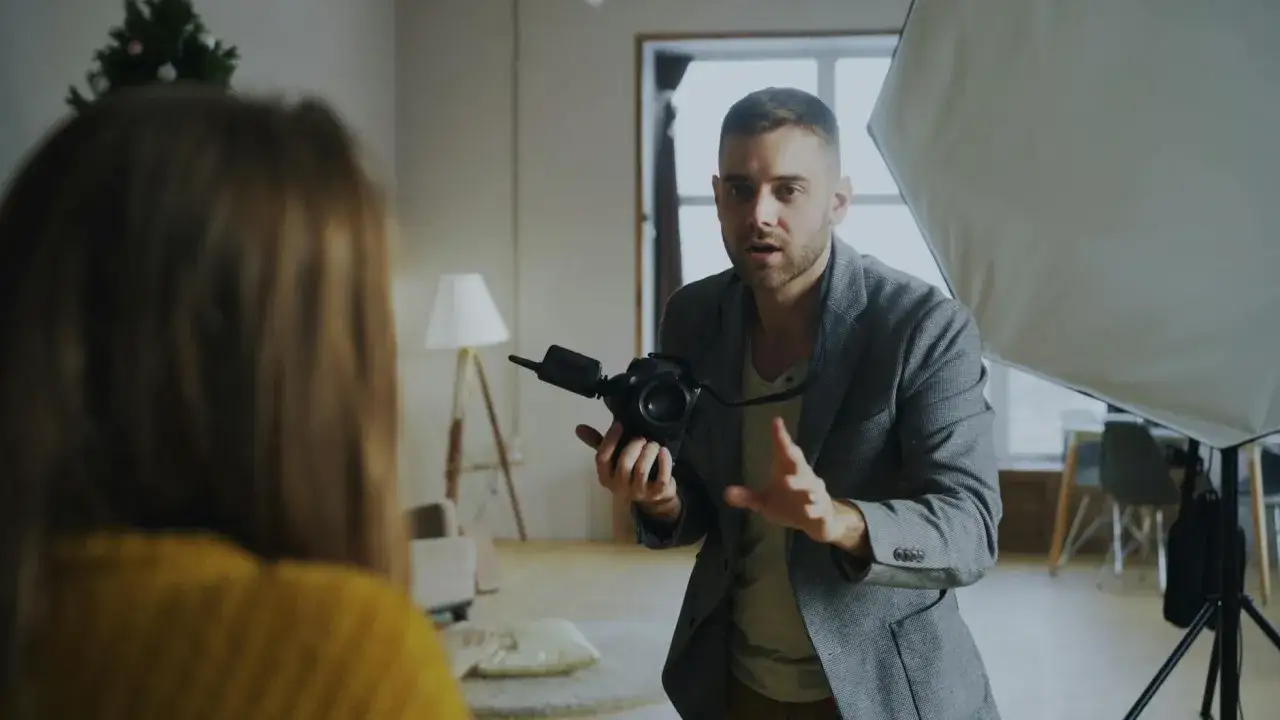 Mężczyzna z aparatem w ręku, w eleganckim żakiecie, instruuje modelkę. To autoportret fotografia w trakcie sesji.