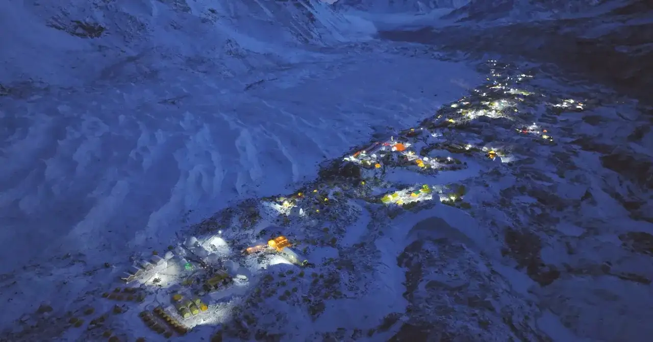 Ein beleuchtetes Zeltlager am Mount Everest, das wie eine kleine Stadt in der eisigen Nacht wirkt. Die Lichter der Zelte leuchten auf der