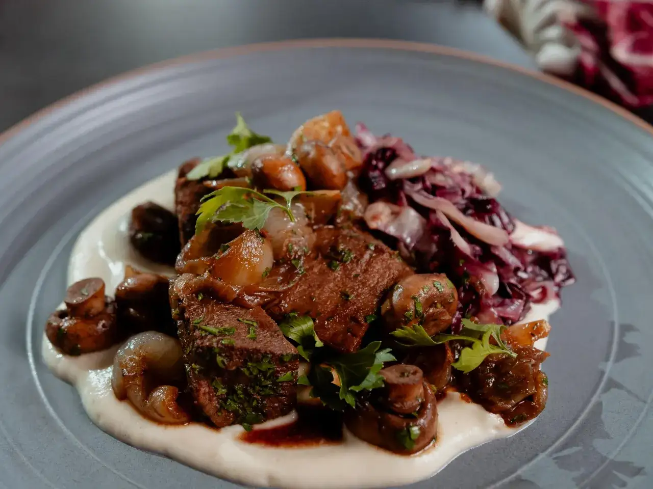 Un plat de langue de bœuf braisée, servie avec des champignons, des oignons caramélisés et une purée onctueuse.