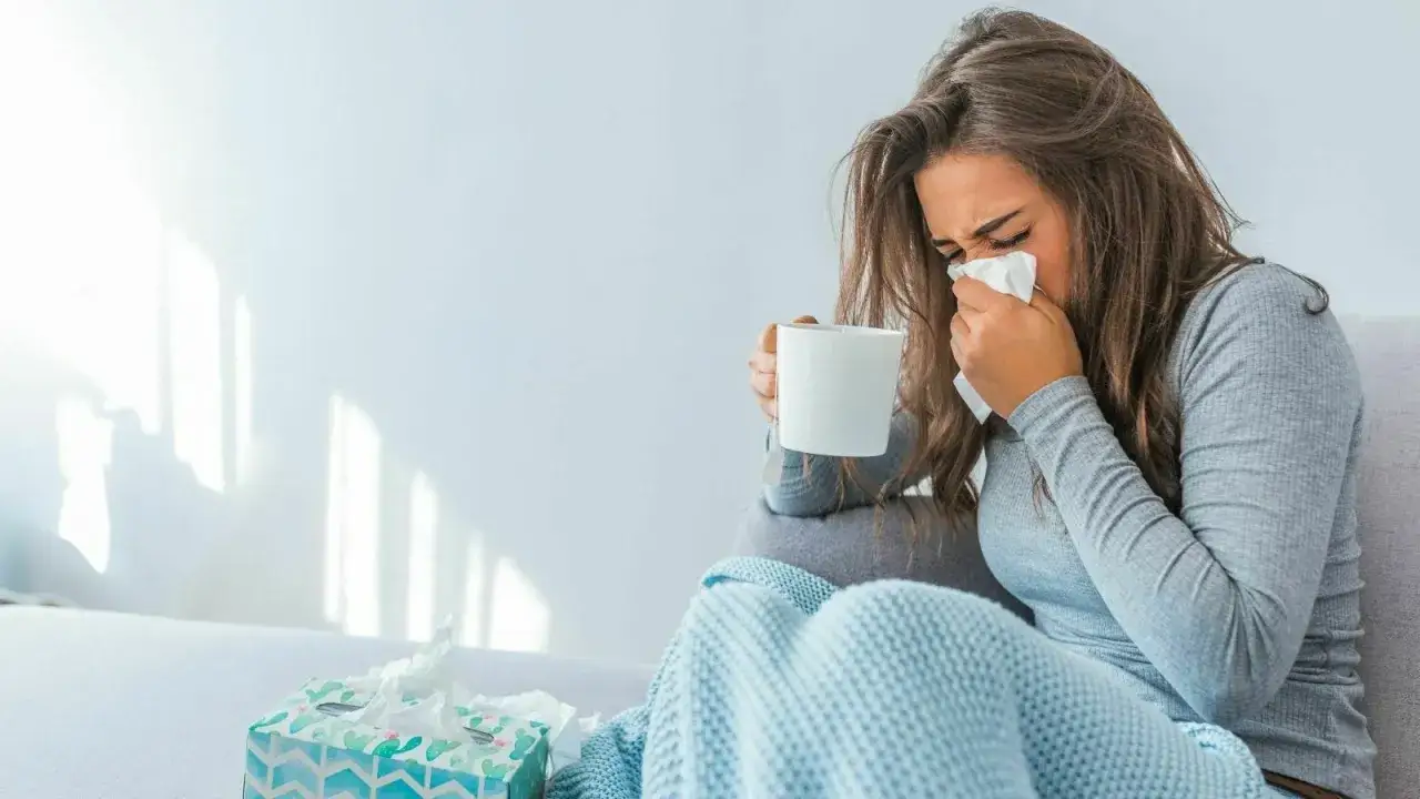 Donna con fazzoletto e tazza, coperta da un plaid. Il suo tirocinio &egrave; interrotto da una malattia.
