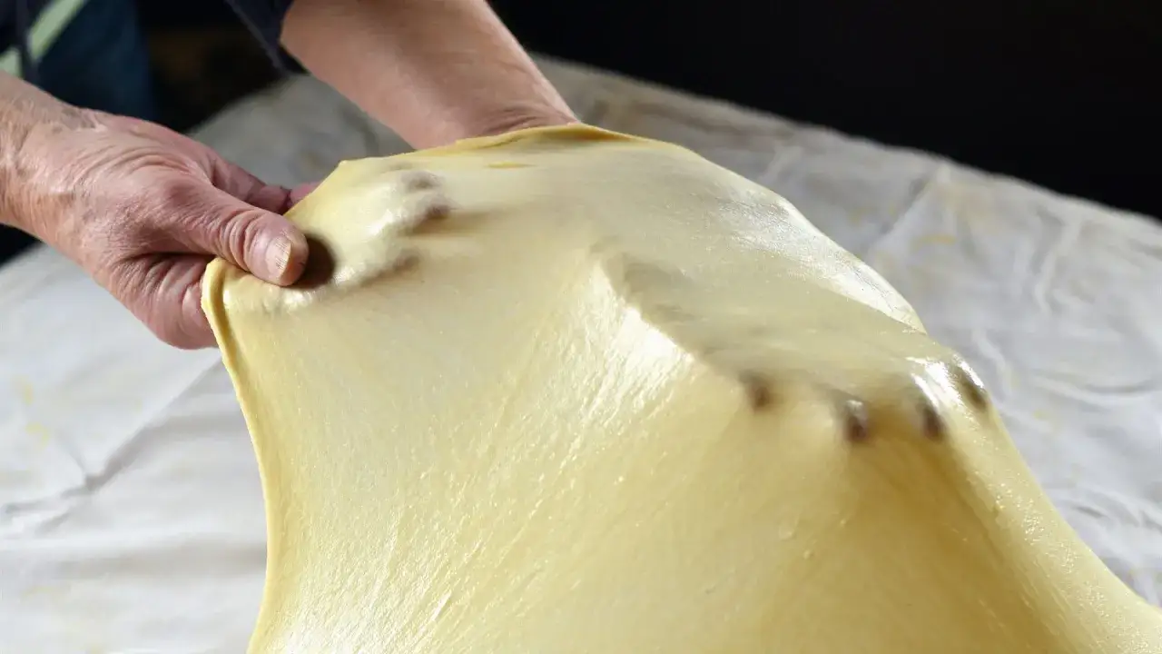 Mani che stendono la pasta matta per una ricetta fatta in casa, mostrando la sua elasticit&agrave;.
