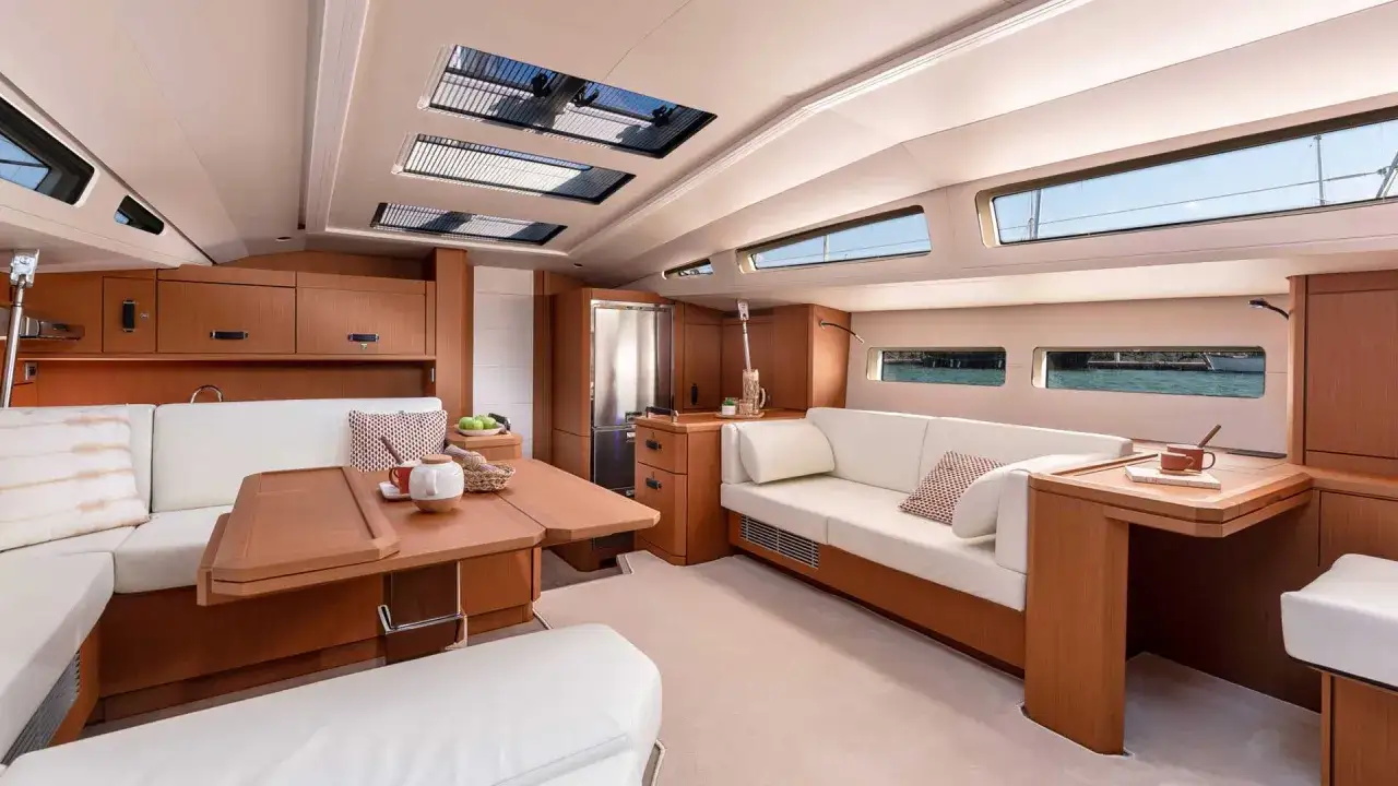 L'élégant **intérieur du voilier** offre un espace de vie lumineux avec des banquettes confortables, une table en bois et de grandes fenêtres donnant sur la mer.
