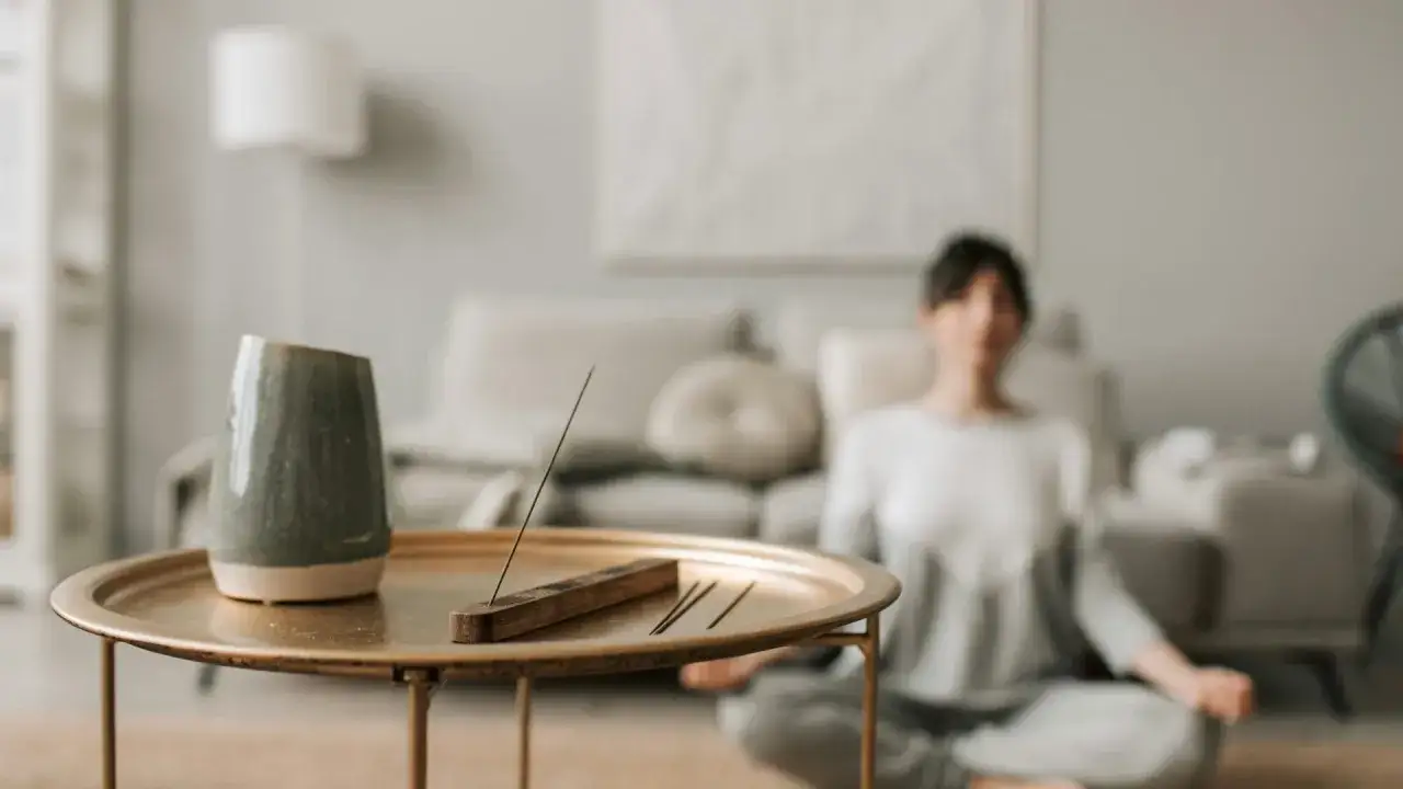 Mujer meditando en postura de loto, con incienso encendido. Un espacio sereno para el bhakti yoga.