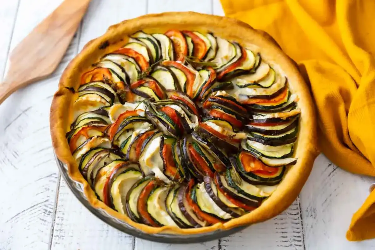 Tarte aux légumes colorée, avec des rondelles de courgettes, aubergines et tomates disposées en spirale sur une pâte dorée.