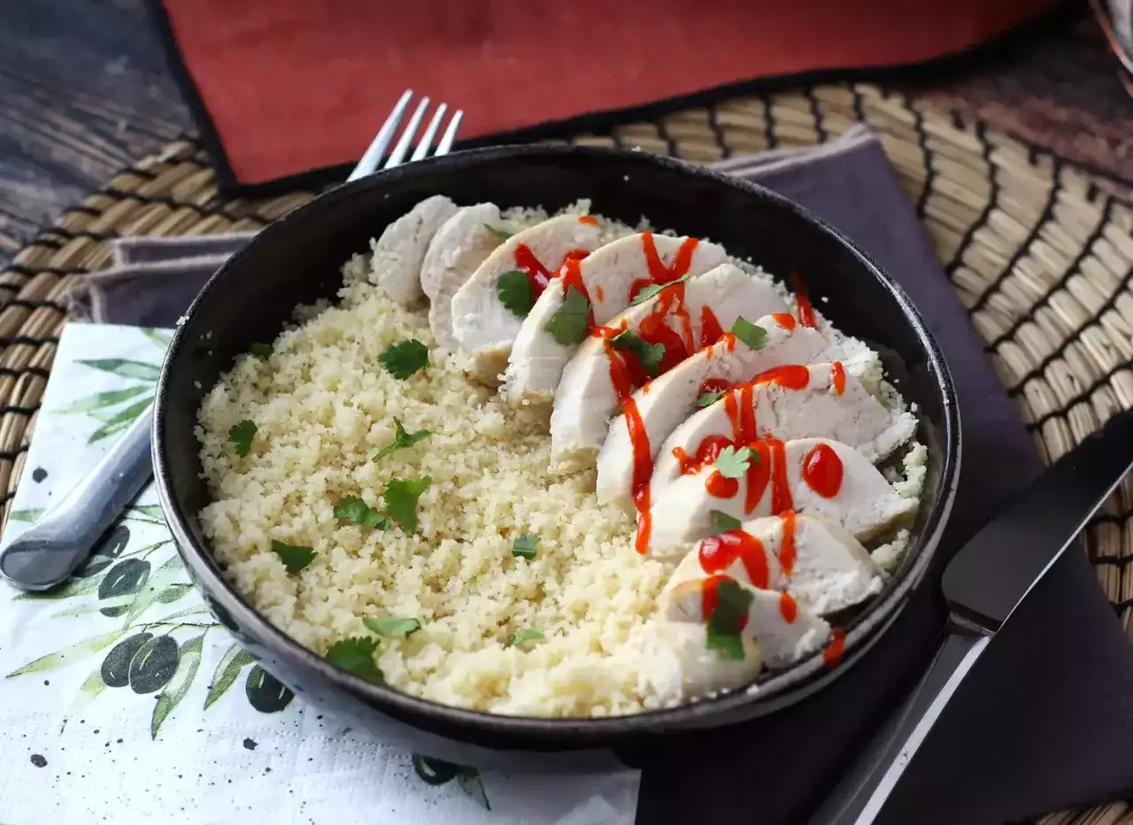 Piatto di couscous con fette di petto di pollo condito con salsa piccante e coriandolo fresco.