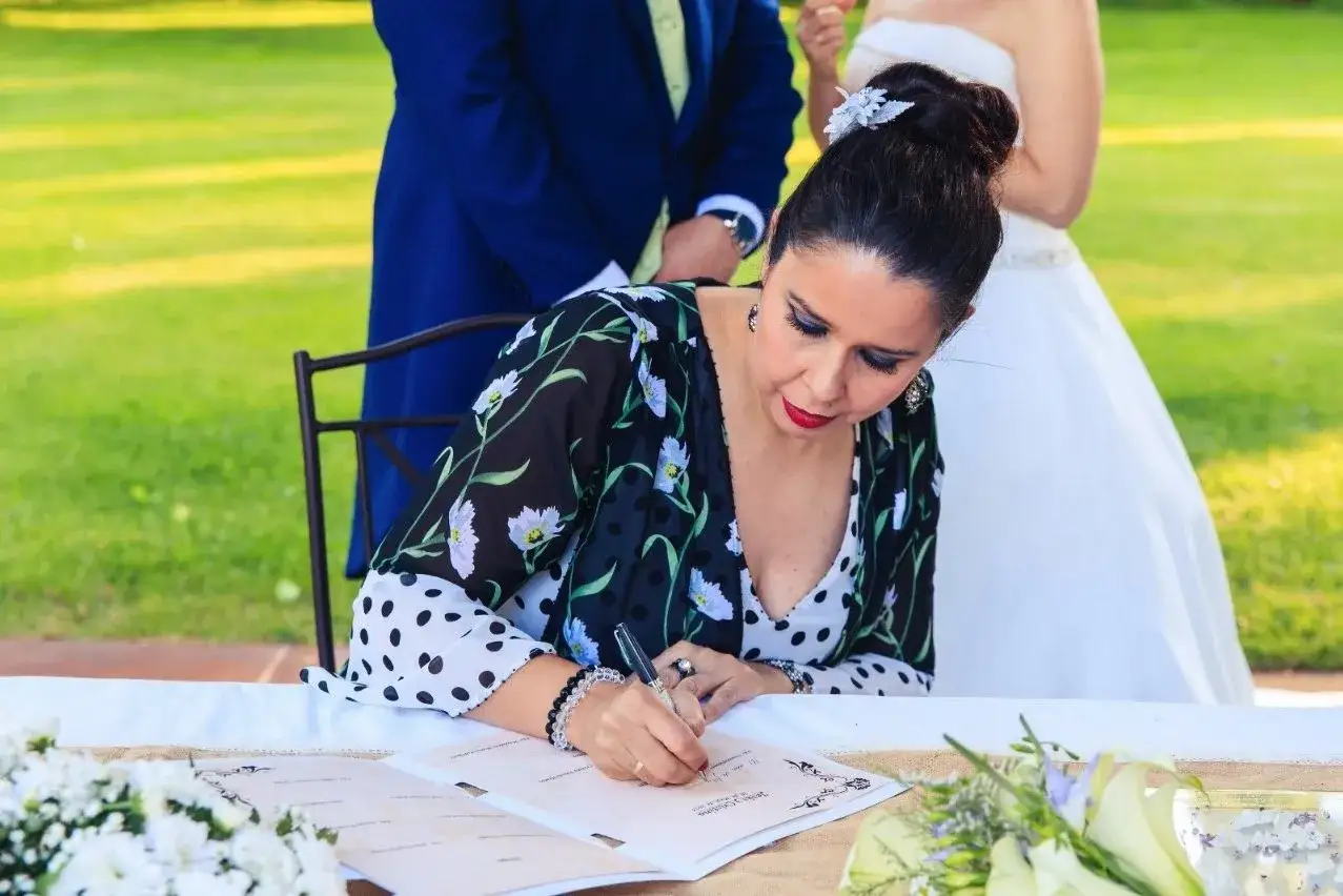 Una mujer firma como testigo en una boda civil. Detr&aacute;s, se ven el novio y la novia.
