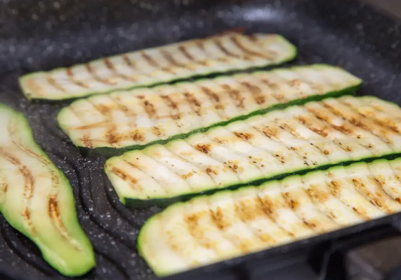 Fette di zucchine grigliate su una piastra, con striature dorate e un contorno verde brillante.