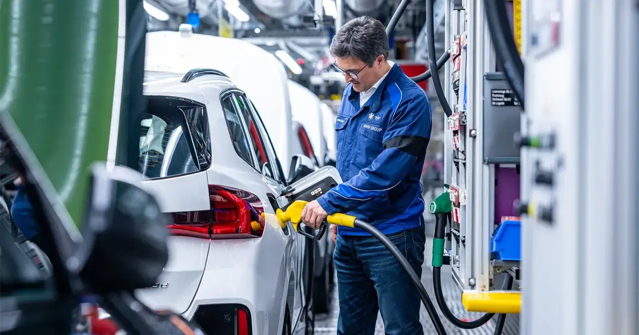 Pracownik BMW tankuje białe auto, prawdopodobnie model BMW 535d, na linii produkcyjnej.