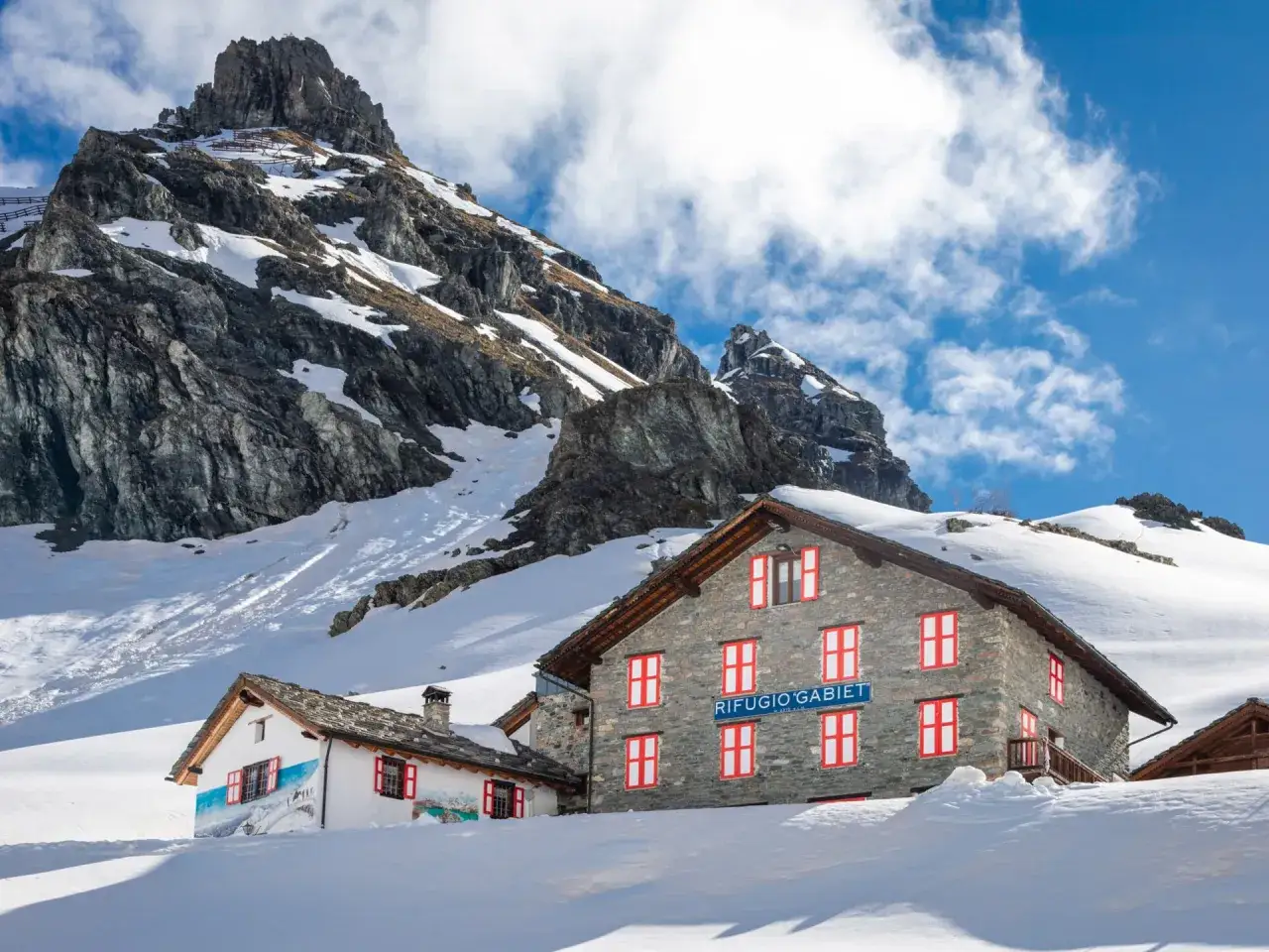 Rifugio Gabiet, un accogliente rifugio in Valle d'Aosta, immerso nella neve con imponenti montagne sullo sfondo.