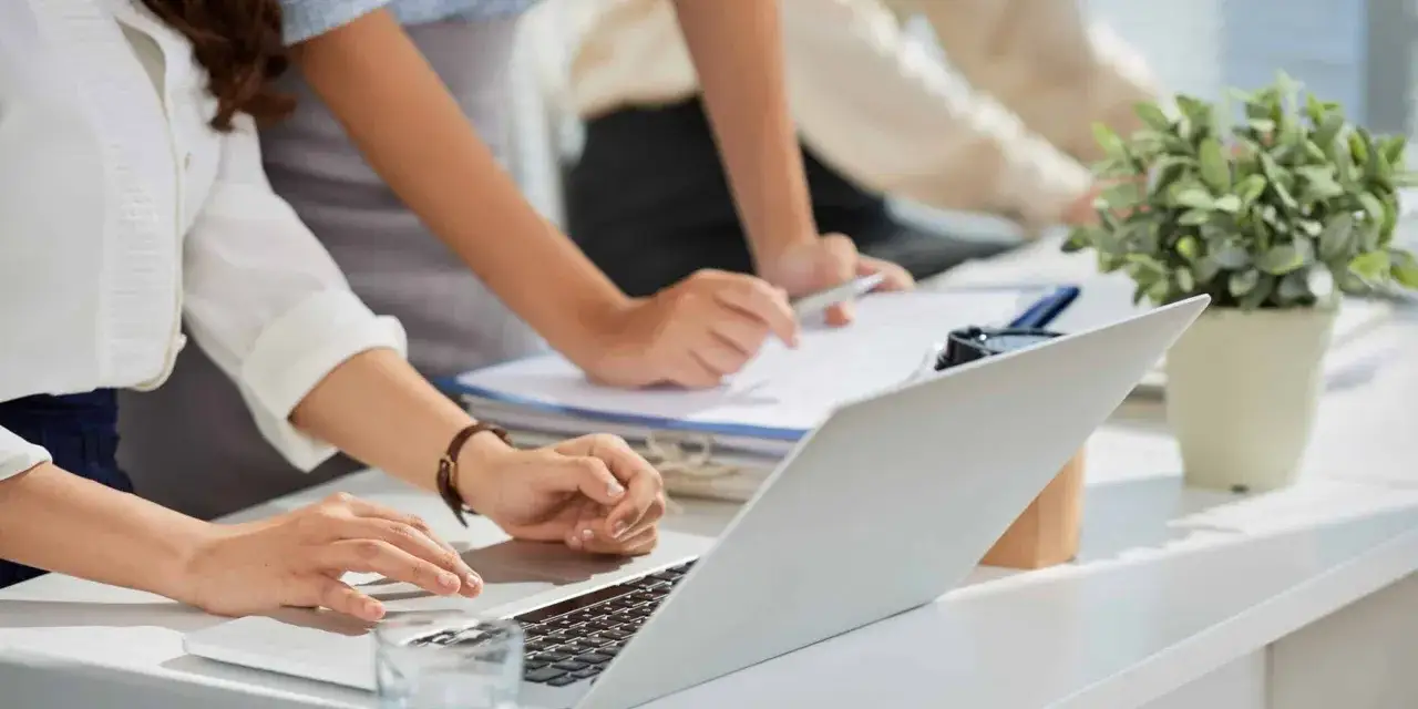 Manos trabajando en un portátil y un documento, reflejando el **código de ética de una empresa** en un entorno de oficina colaborativo.
