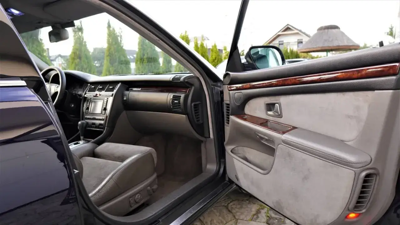 Wnętrze Audi A8 D2 4.2 z drewnianymi wstawkami i skórzaną tapicerką. Widok na deskę rozdzielczą i drzwi.