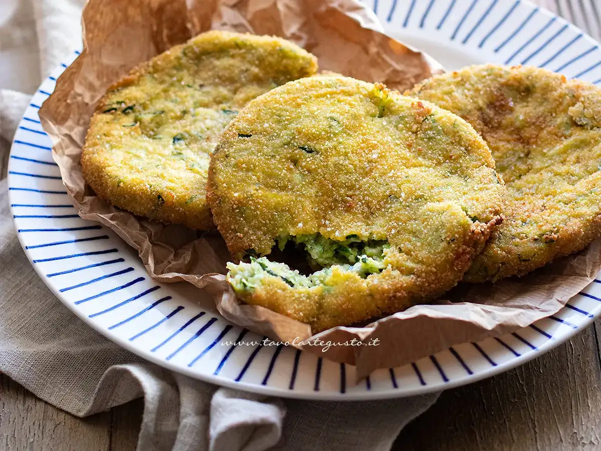 Tre cotolette di zucchine dorate e croccanti, servite su un piatto a righe blu.