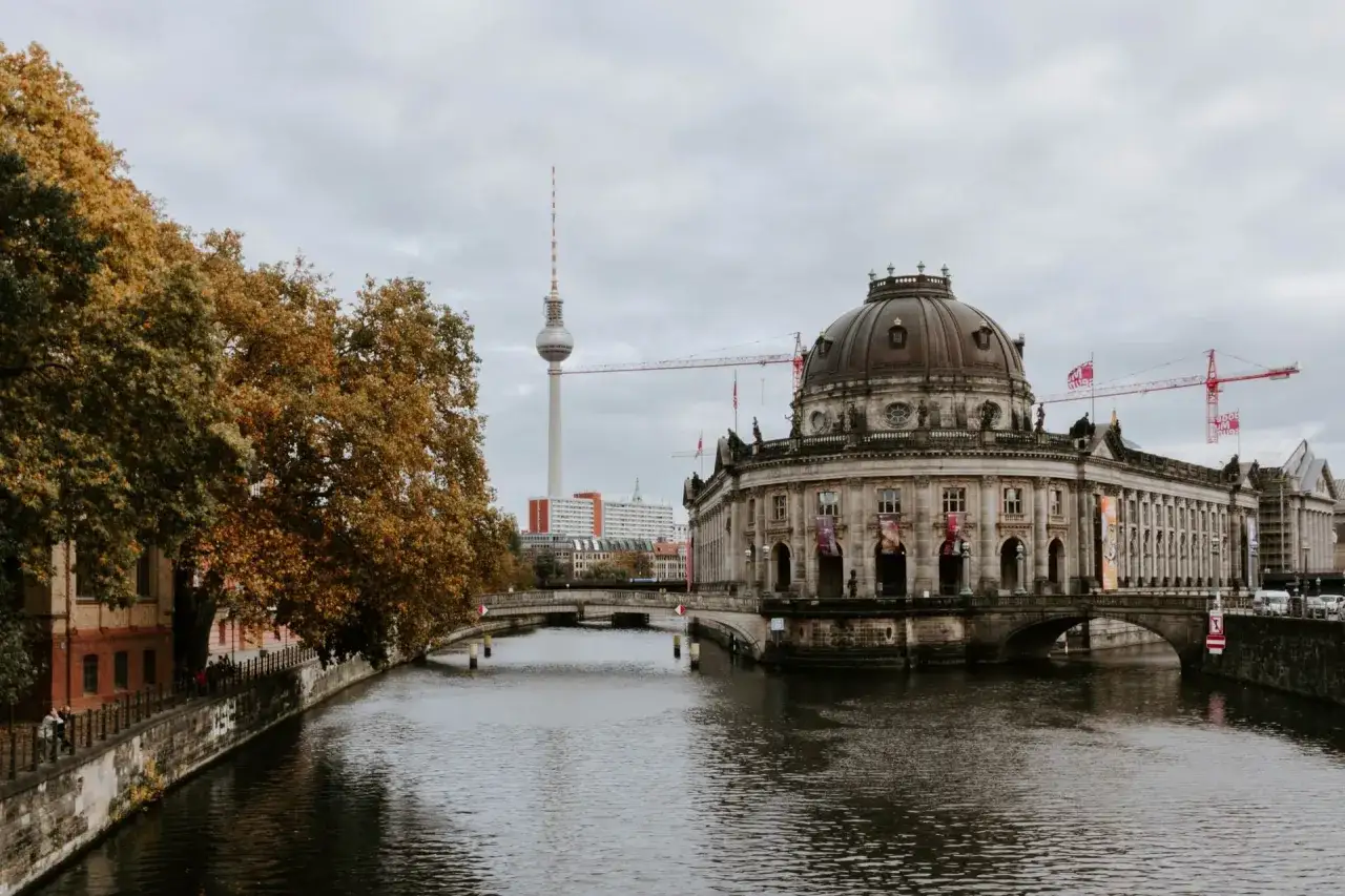 Jesienny Berlin nad rzeką. W tle wieża telewizyjna i budynki, a obok zabytkowa kopuła. W oddali widać żurawie budowlane, jakby przygotowywano się do przyjazdu niemieckich pociągów.