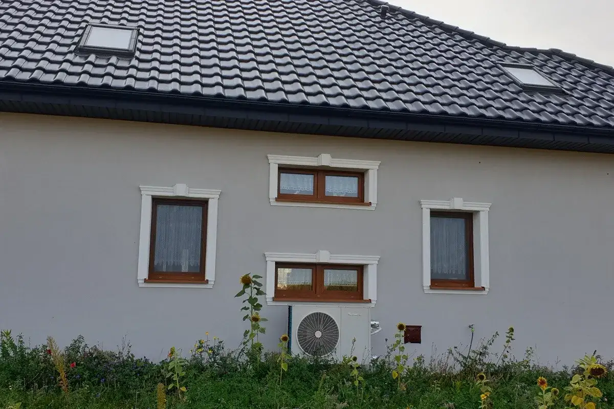 Elegancki gzyms zdobi okna domu, nadając mu stylowy wygląd. Pod oknami kwitną słoneczniki.