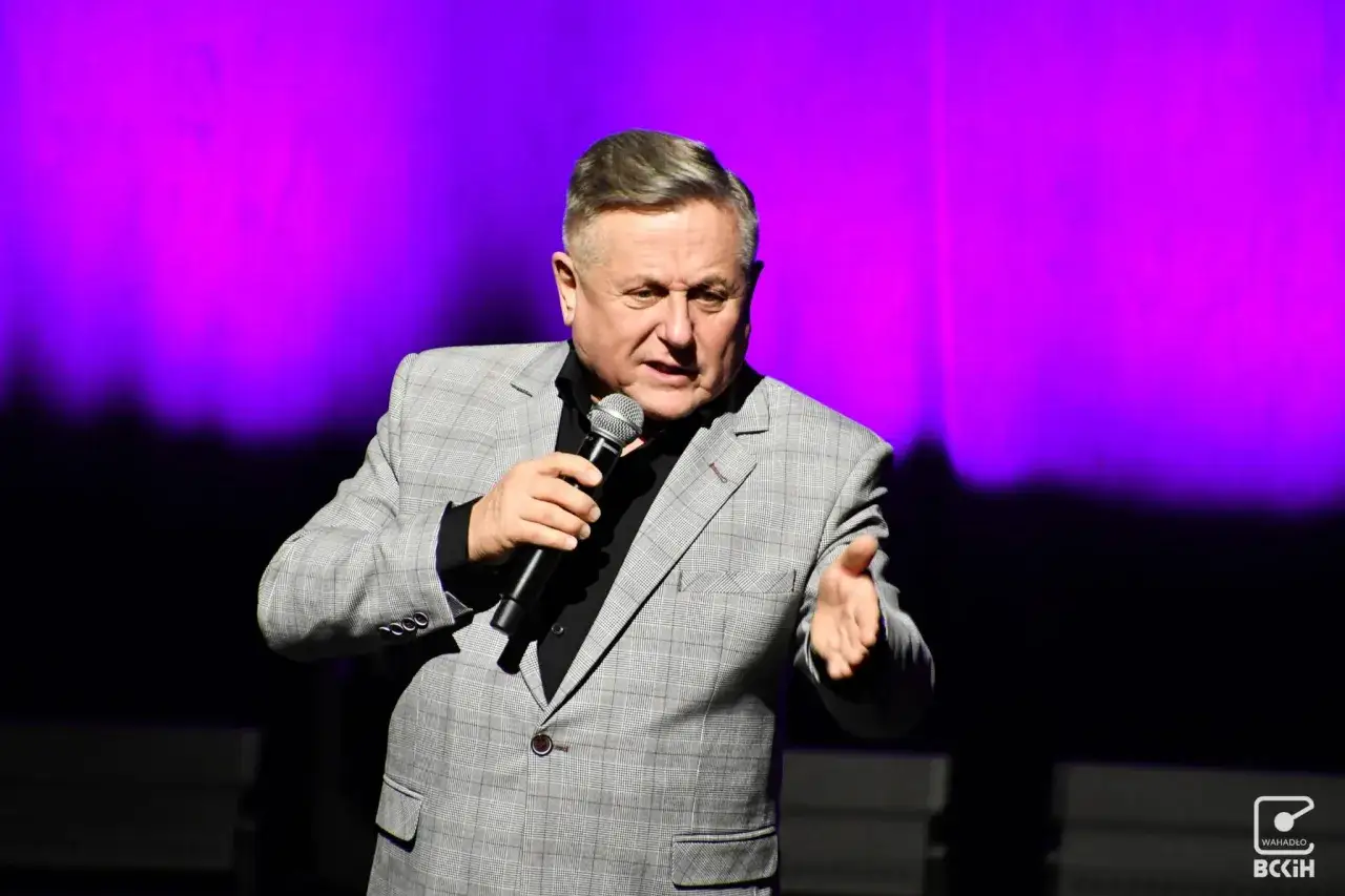 Mężczyzna w garniturze, z mikrofonem w dłoni, opowiada dowcipy. To Bercik, znany z występów kabaretowych.