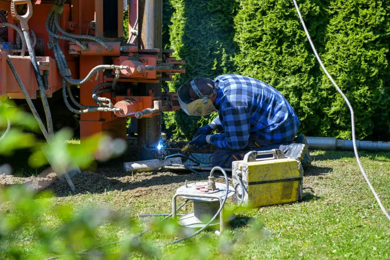 Pracownik w masce spawa elementy wiertnicy, która pomoże jak znaleźć wodę na działce.