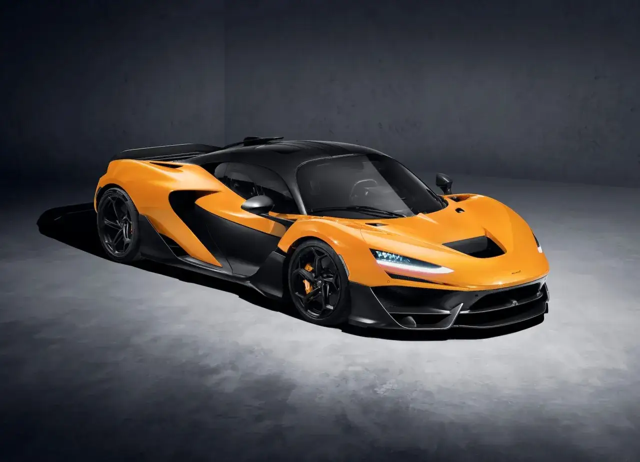 Pomarańczowy McLaren P1 z czarnym dachem i detalami, stojący na betonowej podłodze.