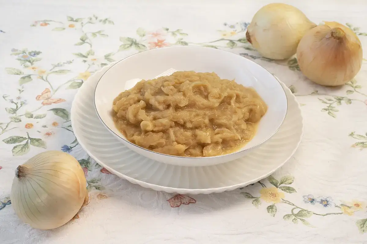 Cebolla caramelizada en un plato, lista para deliciosas recetas con cebolla. Tres cebollas crudas completan la escena.