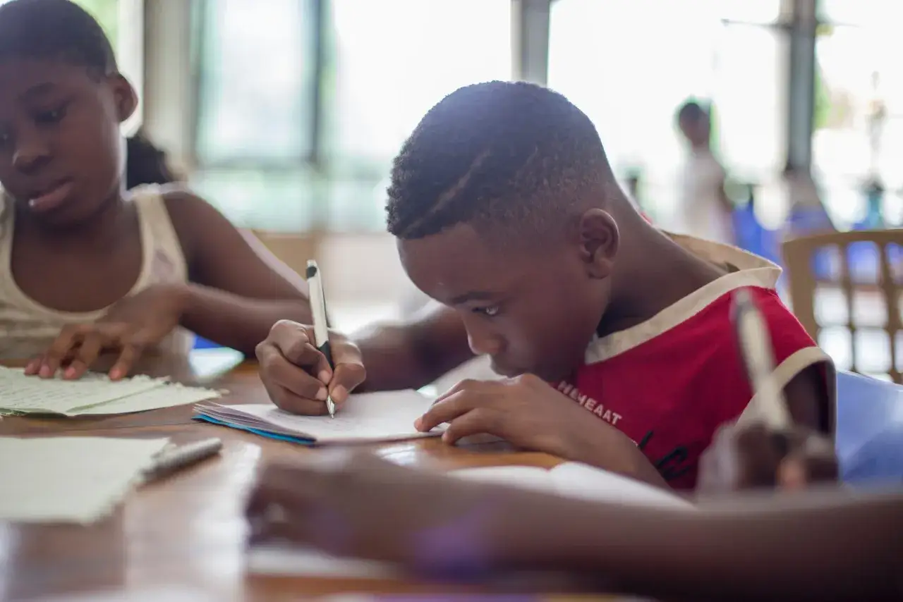 Bambini concentrati scrivono su fogli. Il peer tutoring cos'&egrave;? &Egrave; imparare insieme, aiutandosi a vicenda, come fanno questi studenti.