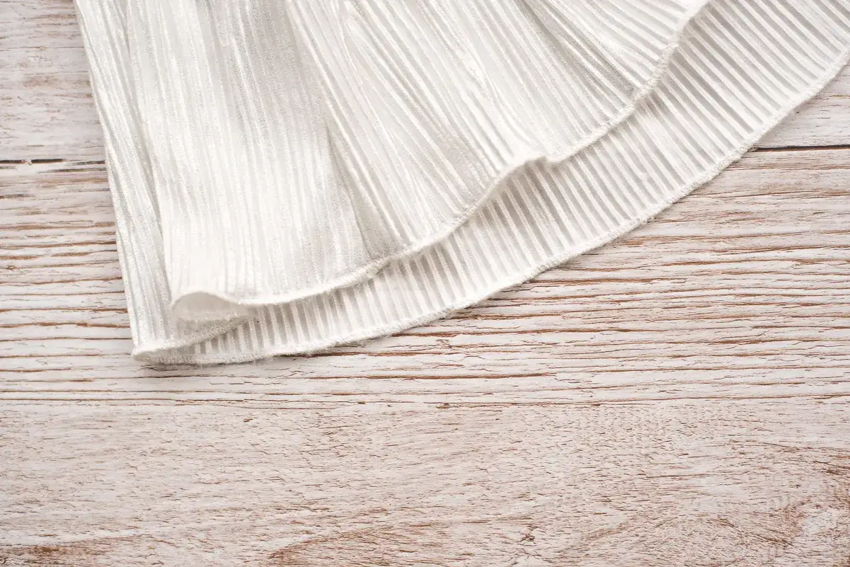 A white pleated fabric with a ruffled hem, showcasing different skirt hem types.