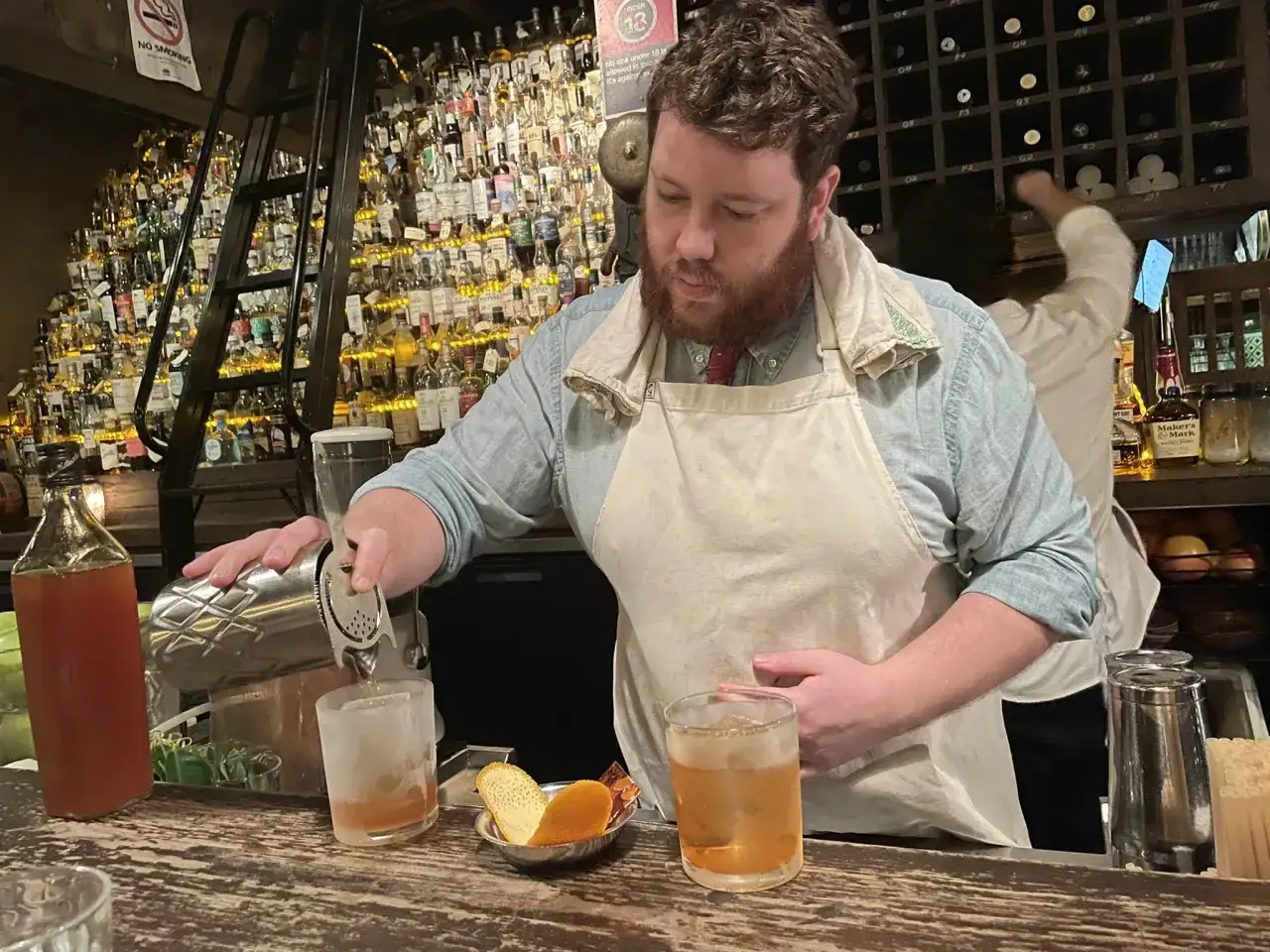 Barman przygotowuje drink z whisky. Na półkach za nim stoją setki butelek alkoholu.