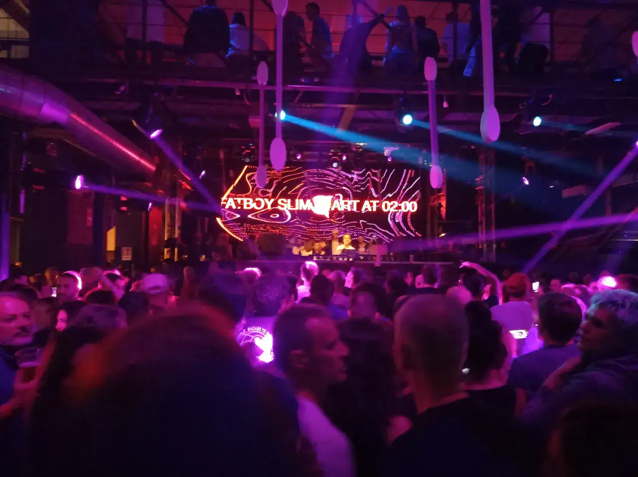 Una folla festeggia a **Torino** di **notte**, illuminata da luci viola e blu. Sullo schermo,