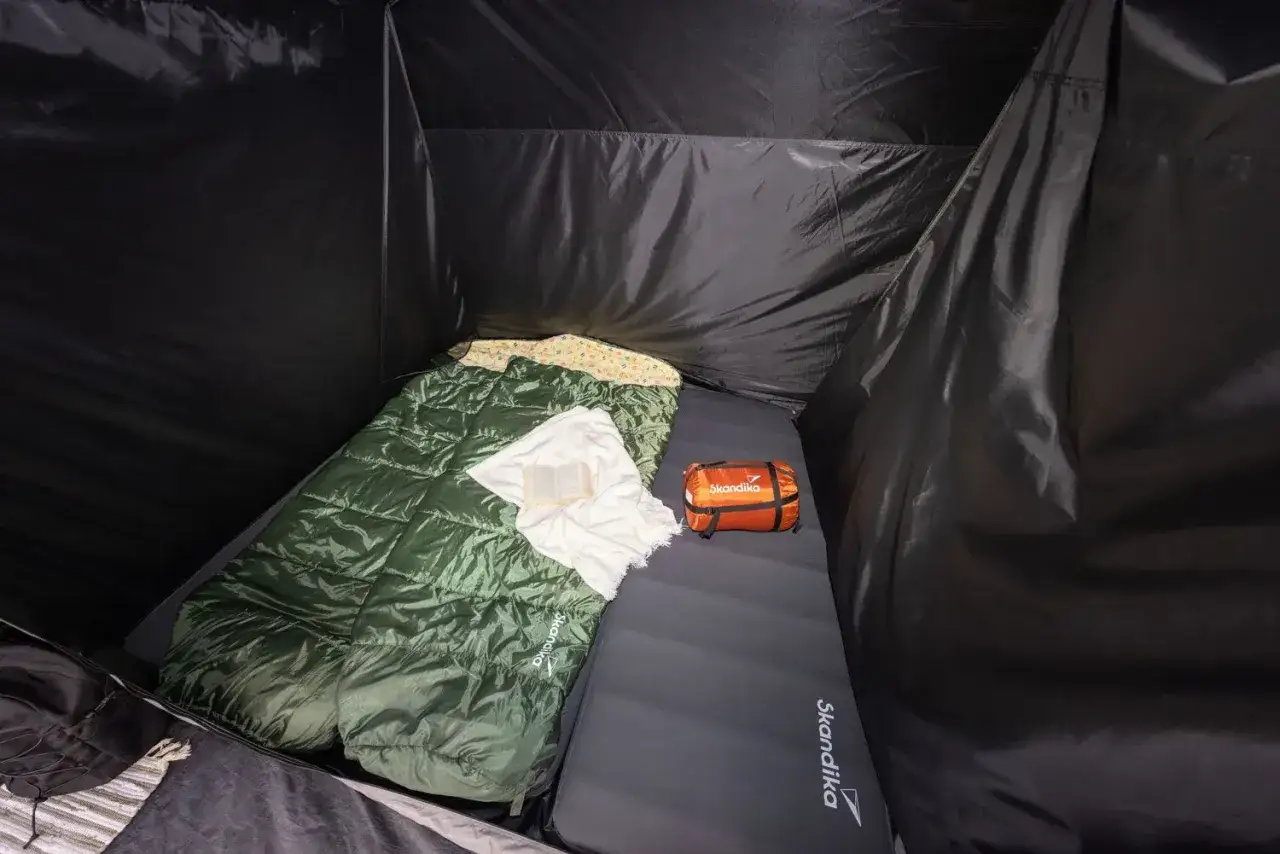 Schlafsack und Kissen auf einer Isomatte, welche Seite oben ist, ist klar erkennbar. Daneben ein kleiner orangefarbener Packsack.