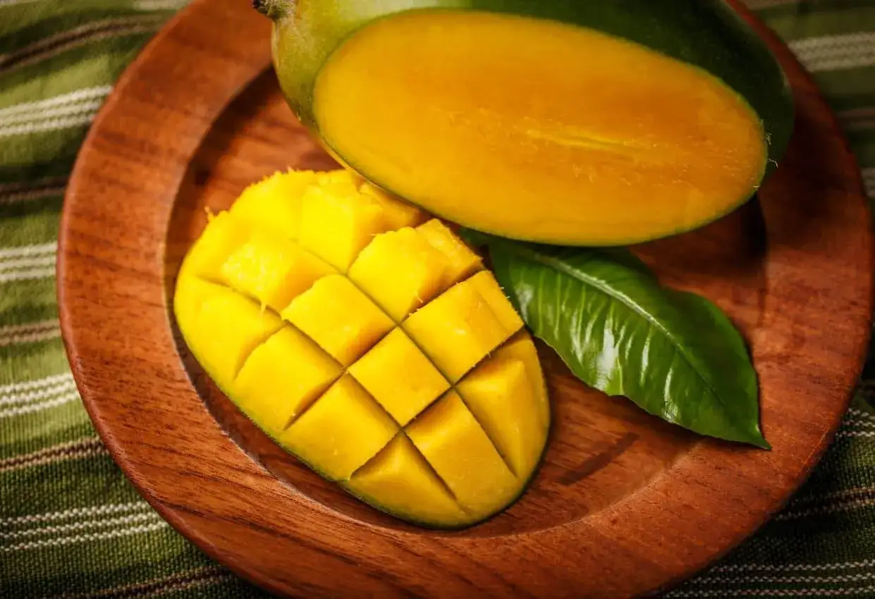 Eine aufgeschnittene Mango auf einem Holzteller. Die Frucht ist leuchtend gelb und saftig. Ist Mango gesund? Ja, sie ist voller Vitamine!