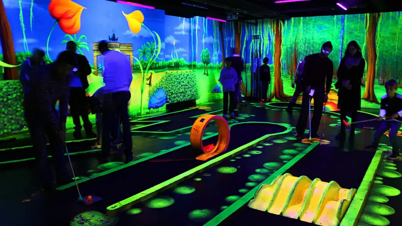 Schwarzlicht Insel Berlin: Familien spielen Minigolf in einer neonbeleuchteten, fantasievollen Welt mit leuchtenden Pflanzen und B&auml;umen.