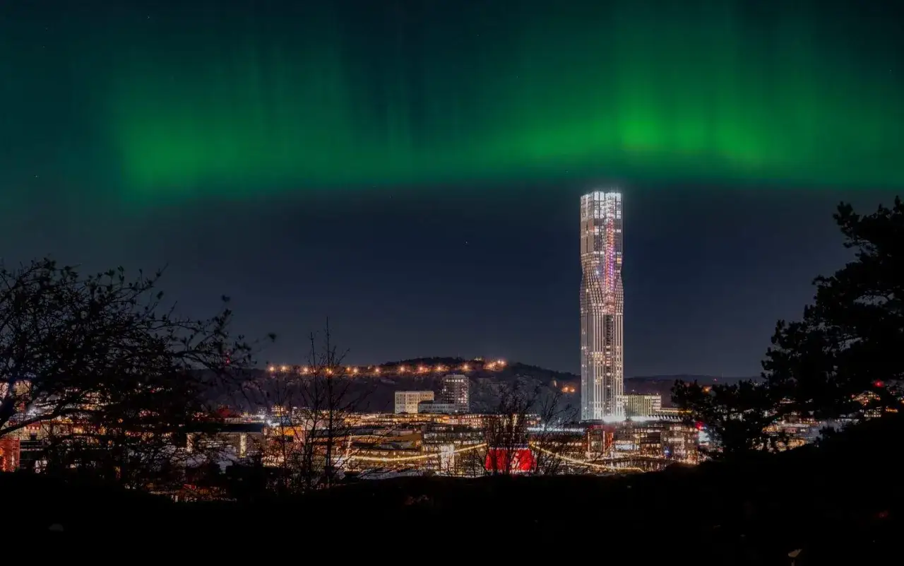 Grön norrsken dansar över Göteborgs silhuett med den ikoniska skyskrapan Lilla Bommen upplyst.