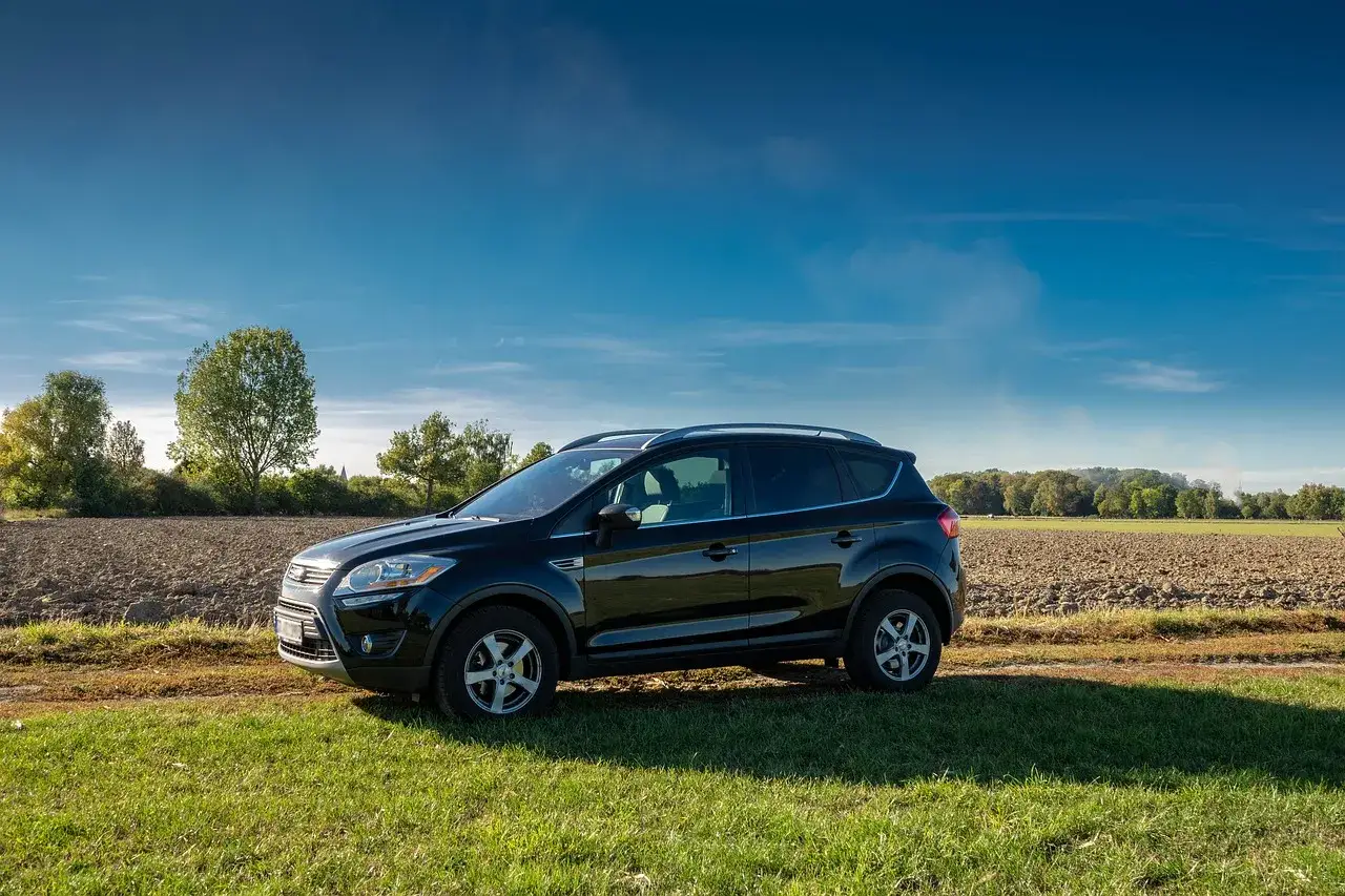 Czarny Ford Kuga na tle pola i drzew. Zastanawiasz się nad jego **ford kuga spalanie**?