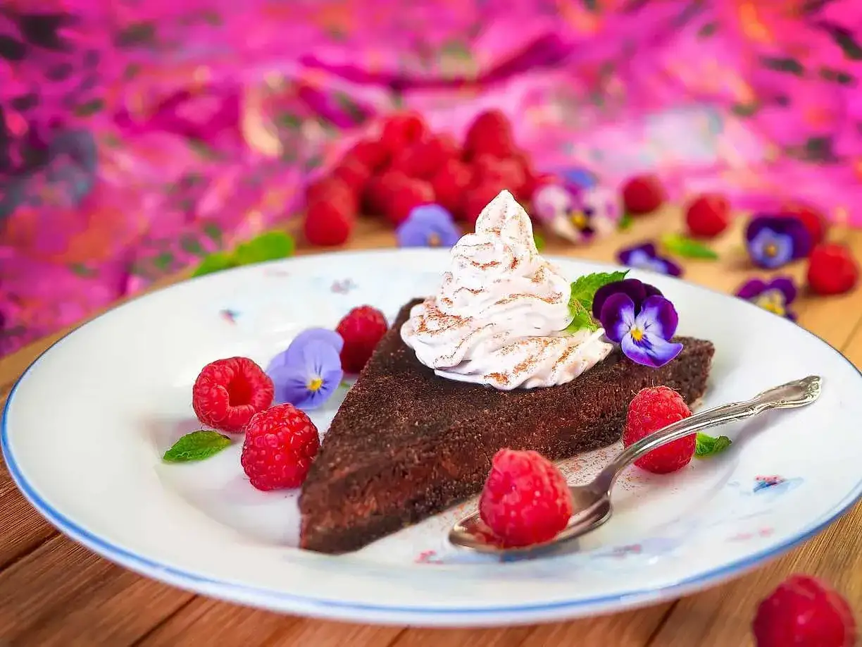 En bit vegansk kladdkaka med fluffig grädde, hallon och violer. En härlig dessert!