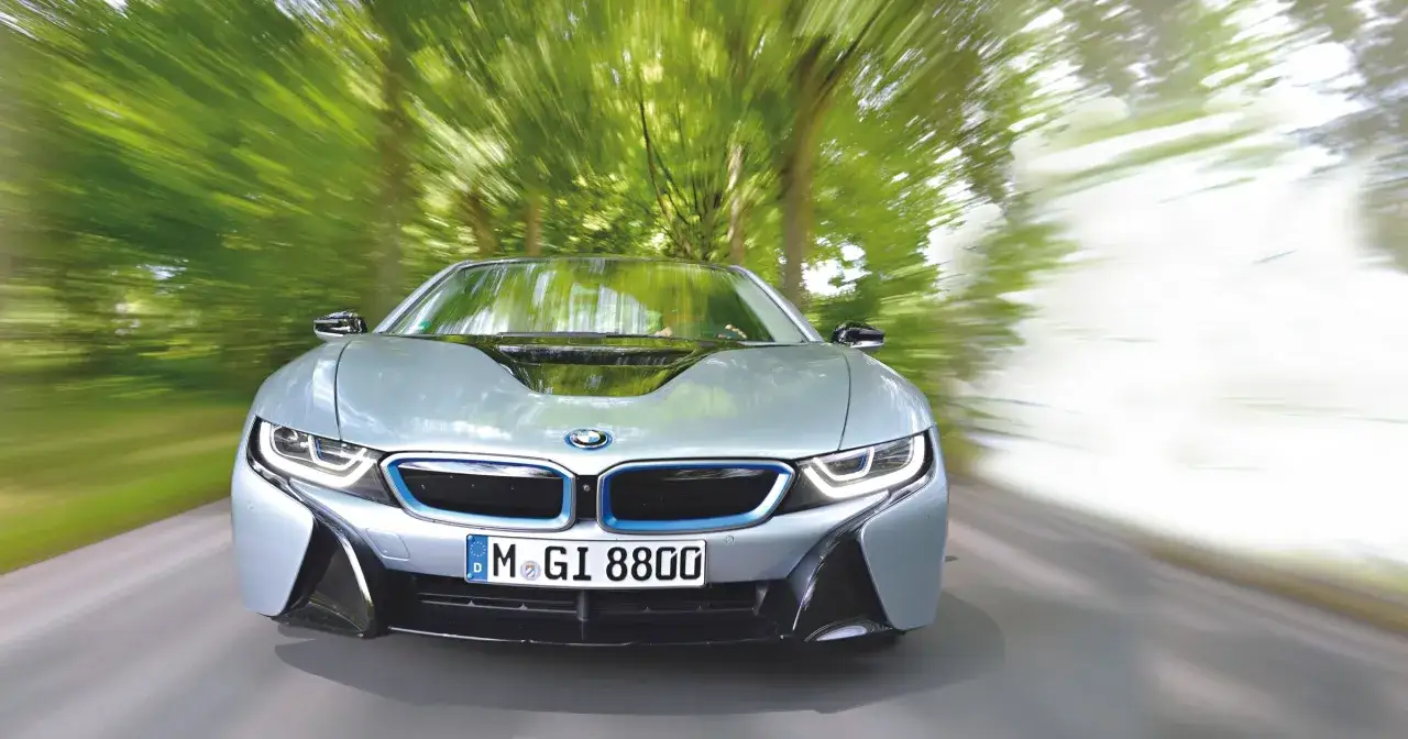 Srebrne BMW i8 pędzi przez zielony las. Sprawdź aktualną bmw i8 cena i możliwości tego sportowego hybrydowego coupe.