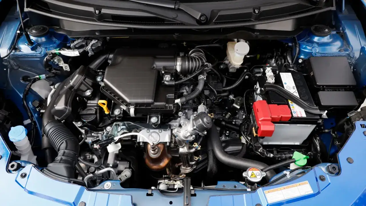 Motorraum eines blauen Suzuki Swift Sport. Viele Kabel und Schläuche, Batterie und Kühlmittelbehälter sichtbar. Keine offensichtlichen Suzuki Swift Sport Probleme hier.