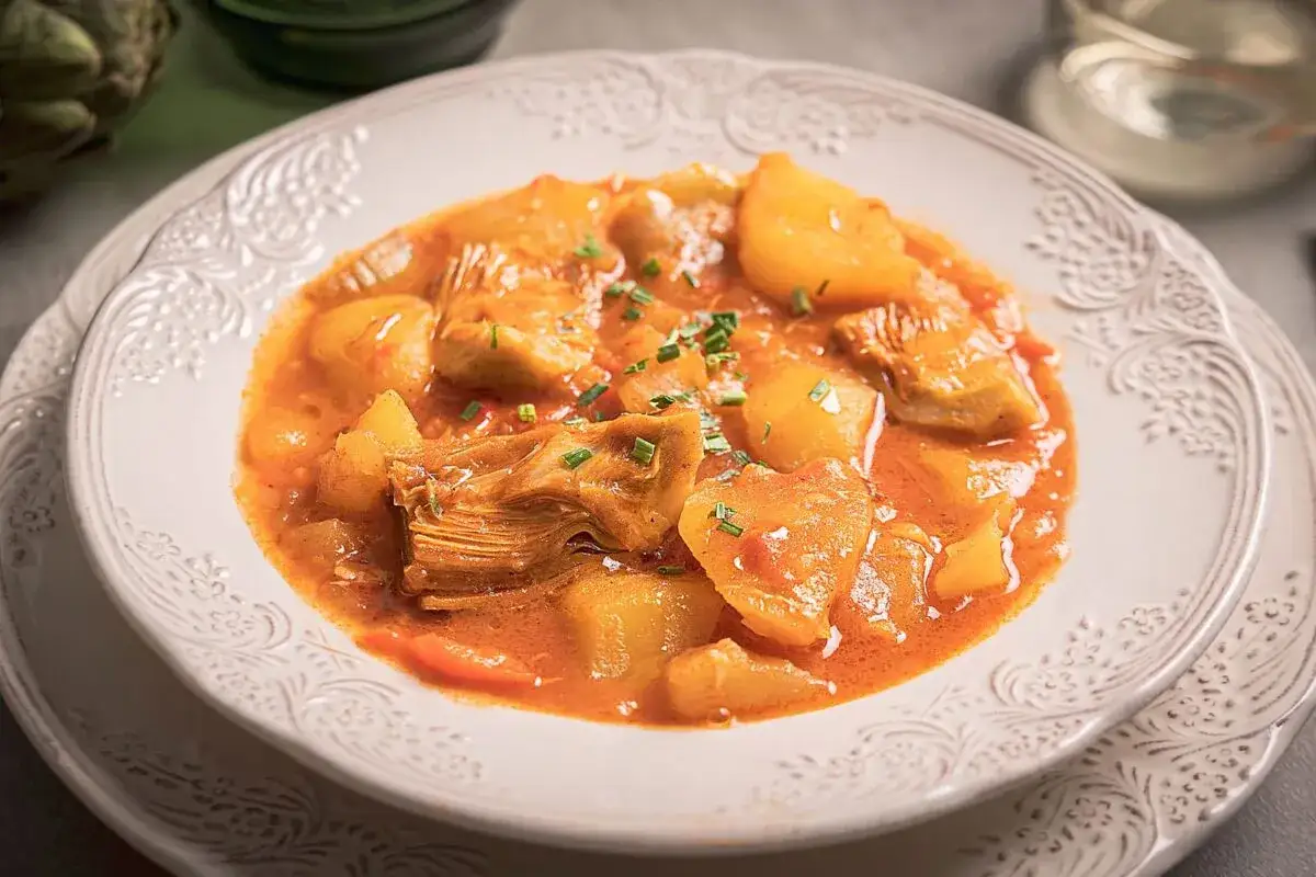 Un plato de guiso de alcachofas con patatas, cubierto con cebollino picado.