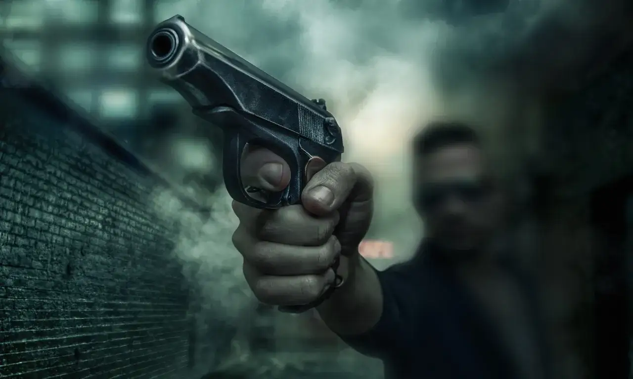 Dłoń trzymająca pistolet, w tle niewyraźna postać mężczyzny. Czy to symbol recydywy, co to znaczy w tym kontekście?