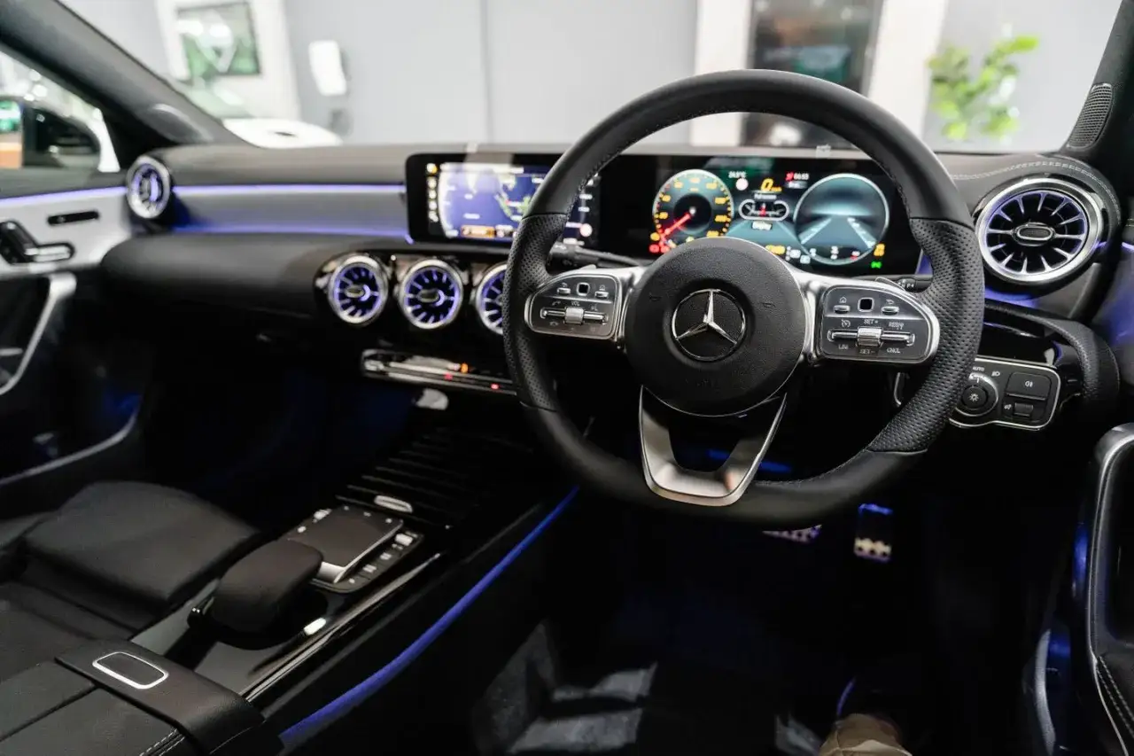 Wnętrze Mercedesa CLA 180: kierownica, cyfrowe zegary i niebieskie podświetlenie tworzą nowoczesny kokpit.