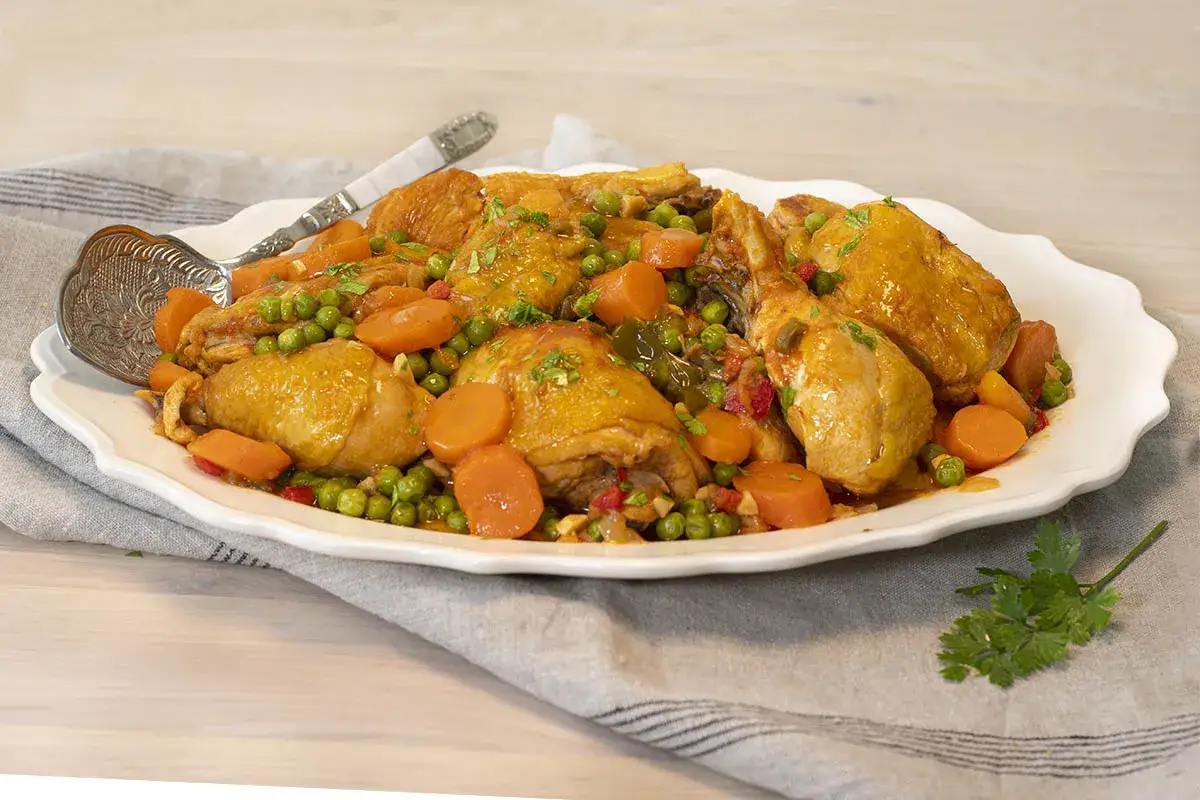 Sabrosas recetas de pollo troceado con zanahorias y guisantes, servido en una fuente blanca con perejil fresco.