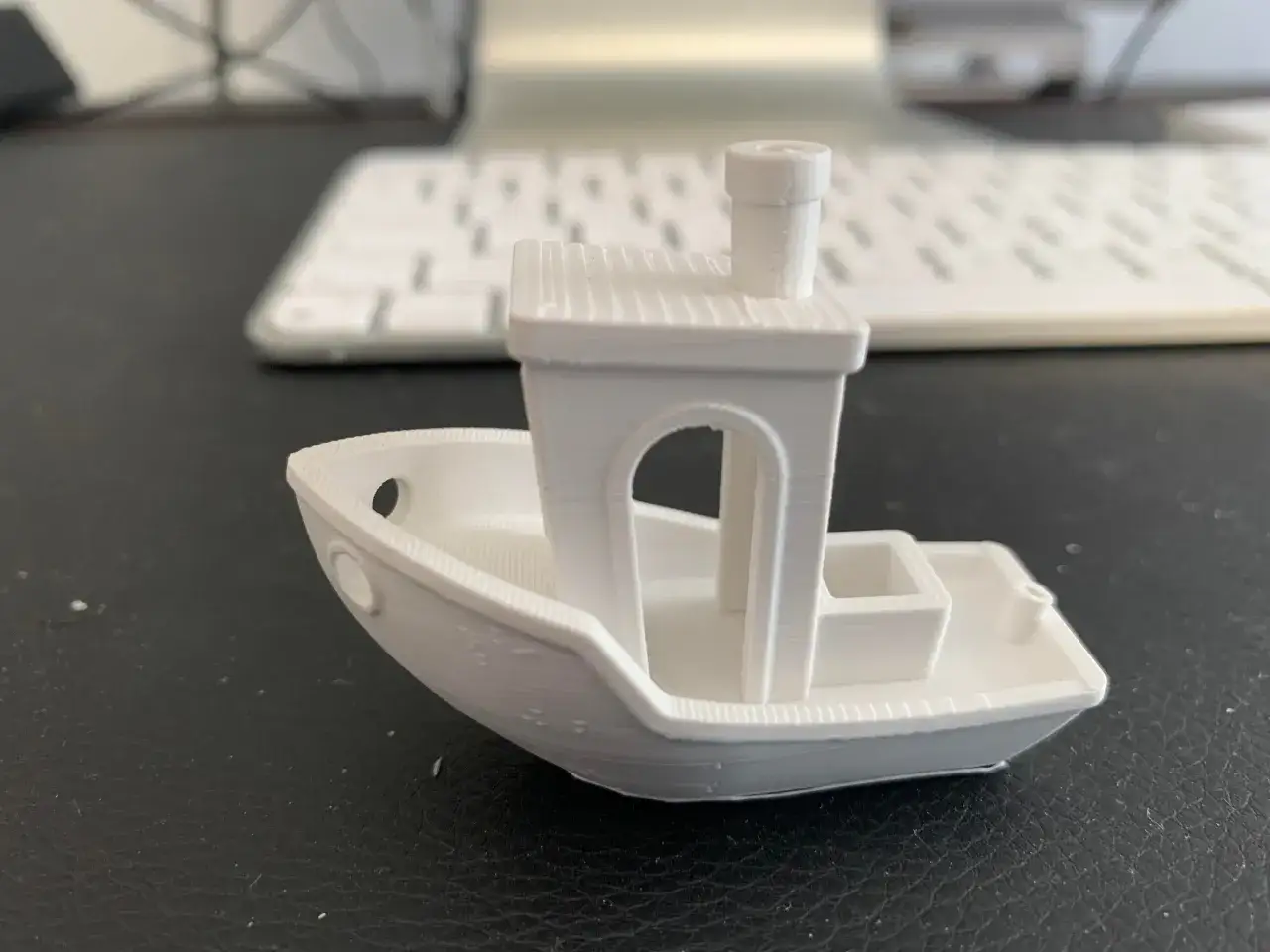 Biała, wydrukowana w 3D łódka, znana jako Benchy, z widocznymi warstwami wydruku, idealny test dla klipper 3d.