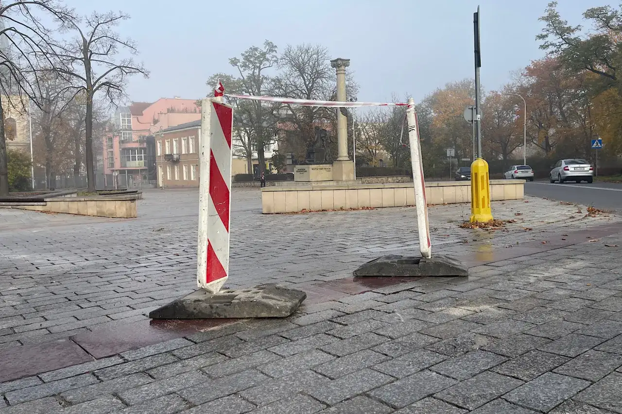 Biało-czerwone słupki z taśmą odgradzają plac z pomnikiem w tle.