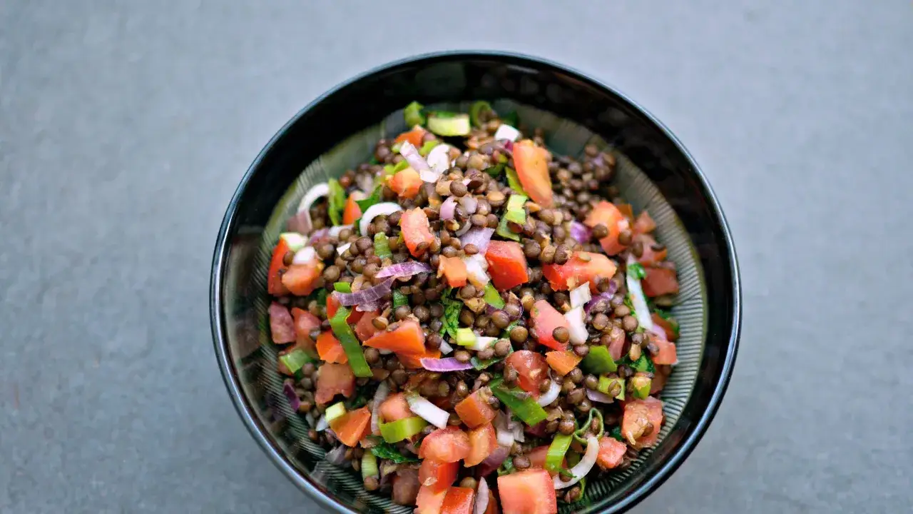 Una ciotola di insalata di lenticchie colorata con pomodori, cipolla rossa e erbe fresche.