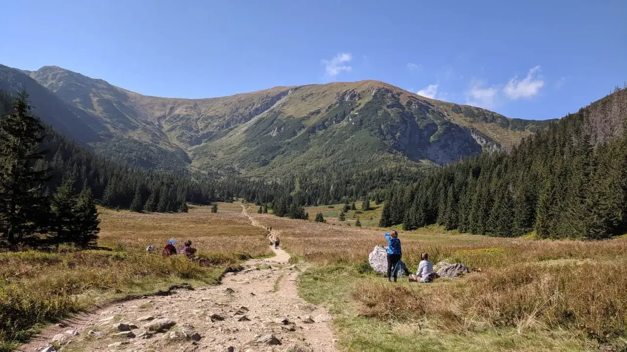 Niebieski szlak na Giewont wije się przez trawiaste doliny i lasy. Ludzie wędrują, podziwiając majestatyczne góry.
