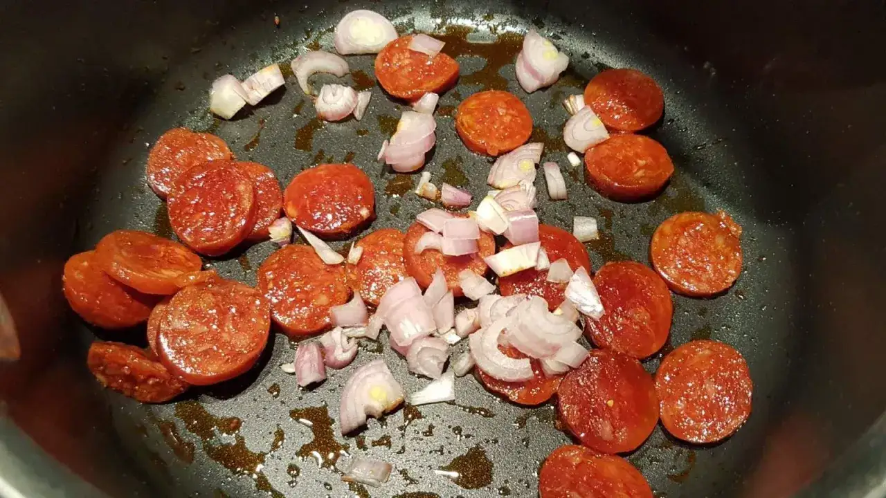 Rondelles de chorizo et &eacute;chalotes coup&eacute;es en d&eacute;s dans une po&ecirc;le, pr&ecirc;tes &agrave; devenir une d&eacute;licieuse sauce chorizo.