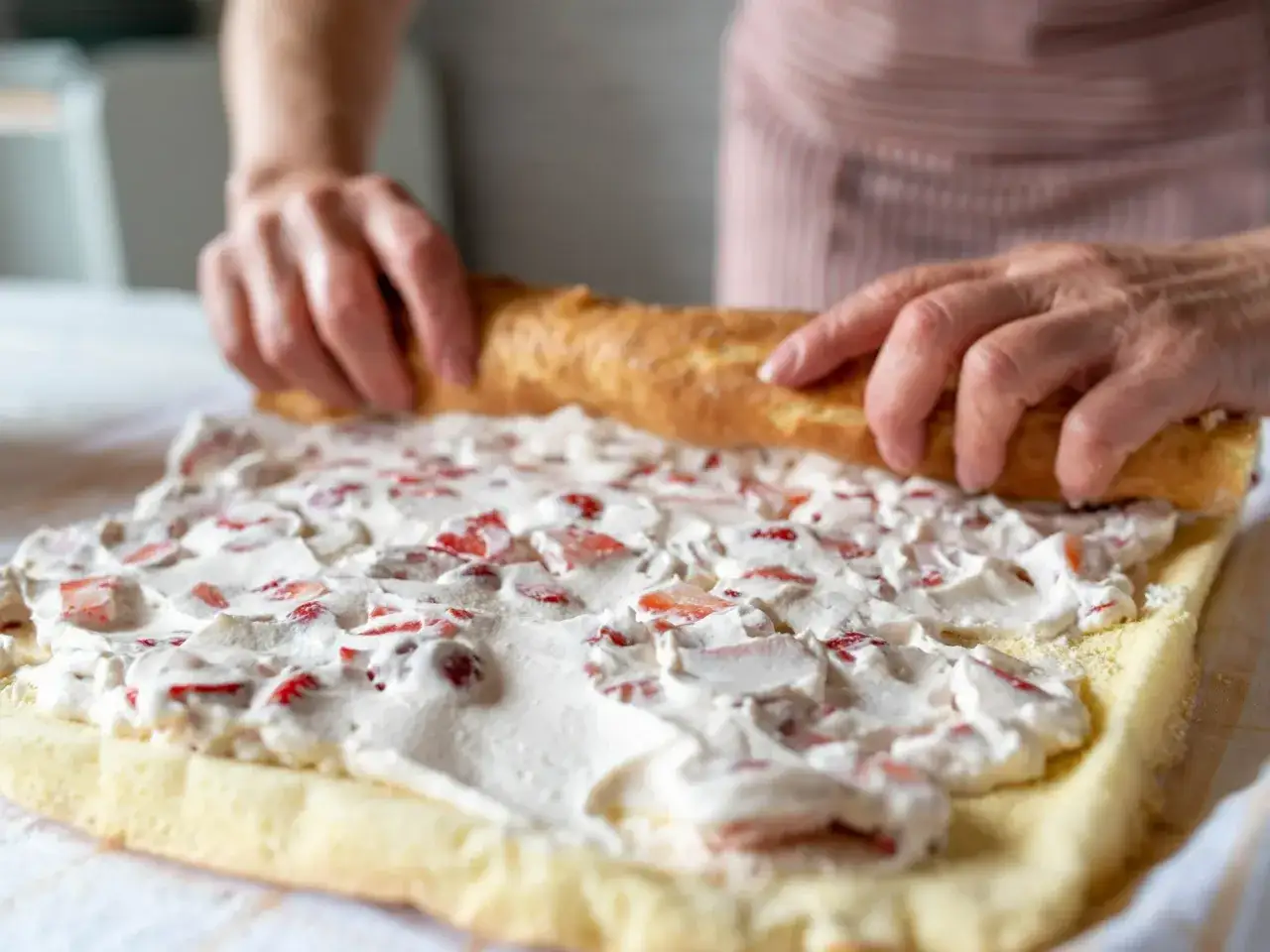 Ręce zwijają biszkopt z kremem truskawkowym. Powstaje najprostsza rolada biszkoptowa, pachnąca latem.
