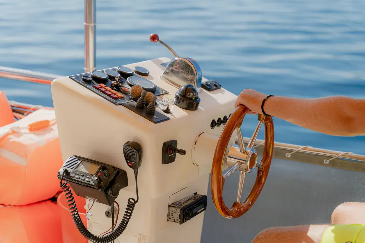 Main d'un homme tenant la roue d'un bateau, pr&ecirc;t &agrave; naviguer. Le tableau de bord du montage commande &agrave; distance bateau est visible, avec des instruments et une radio.