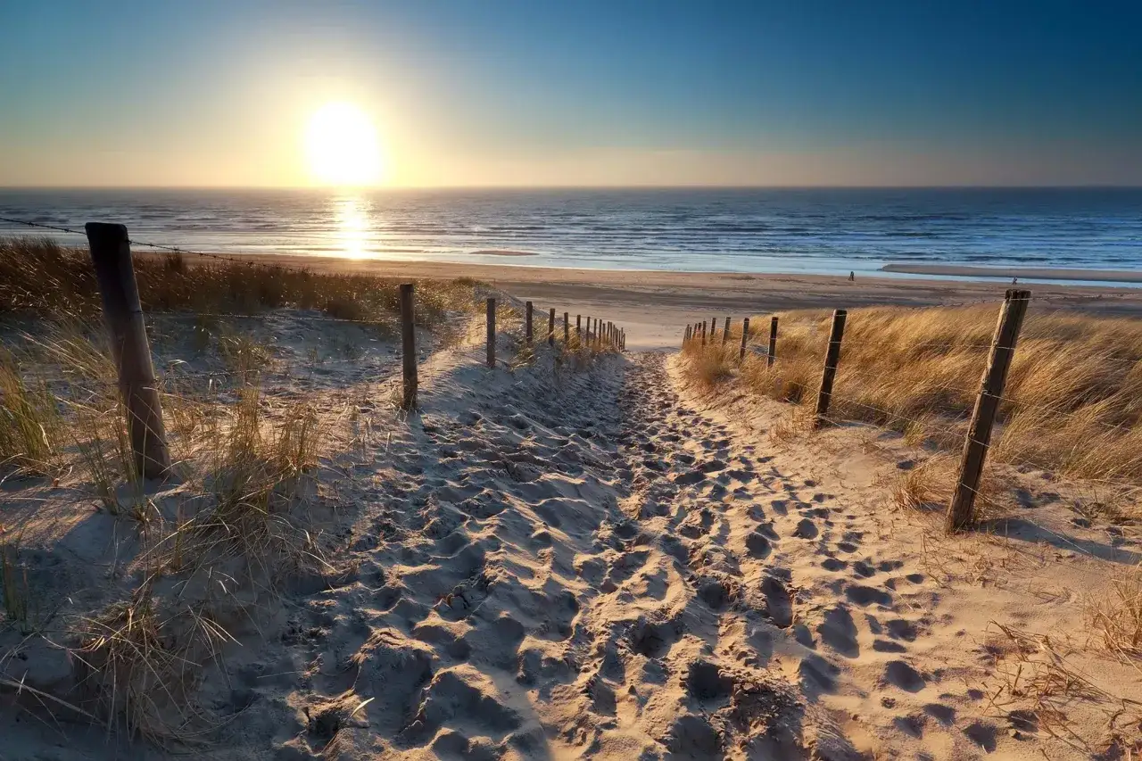 Sonnenuntergang am Strand von Holland. Ein sandiger Weg führt durch Dünen zur Nordsee.