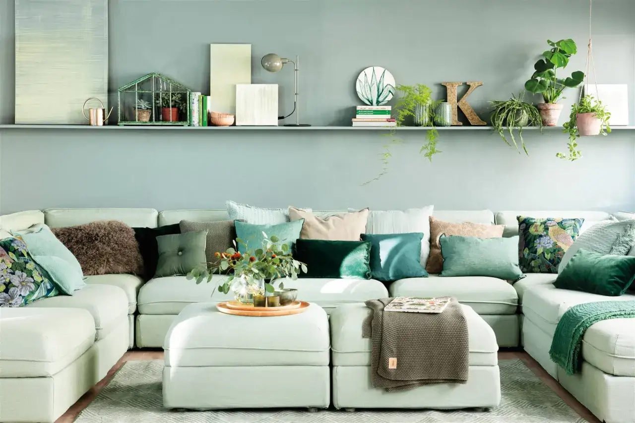 Sofá modular de color verde agua, adornado con cojines en tonos tierra y verdes, creando un ambiente sereno.
