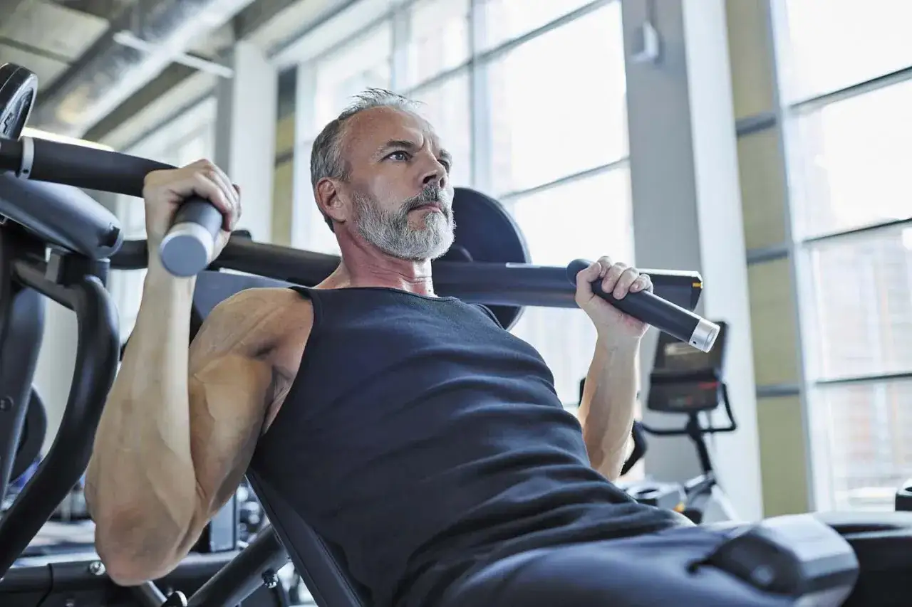 Äldre man med grått skägg tränar axlar på gymmaskin, en del av hans gym program.