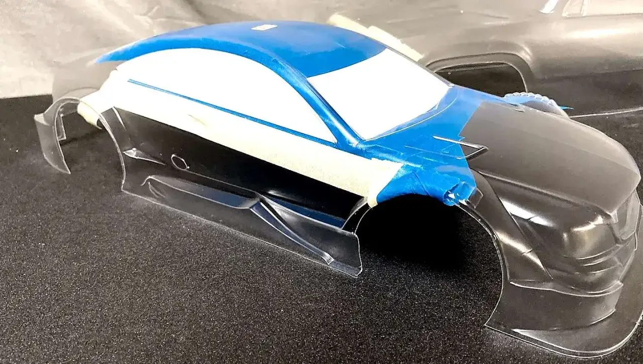 RC-Karosserie wird f&uuml;r das Lackieren vorbereitet. Blaue und wei&szlig;e Farbe sind aufgetragen, Fenster sind abgeklebt.